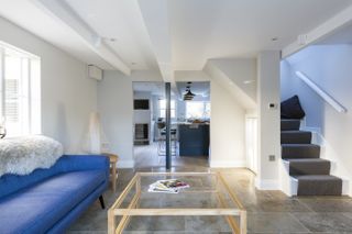 Living space with white walls and blue sofa overlooking staircase and kitchen by Stephen Graver Architects