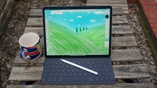 En iPad Pro 12.9 står ute på ett träfärgat bord bredvid en kaffekopp och med sitt tangentbords- och stylustillbehör redo.