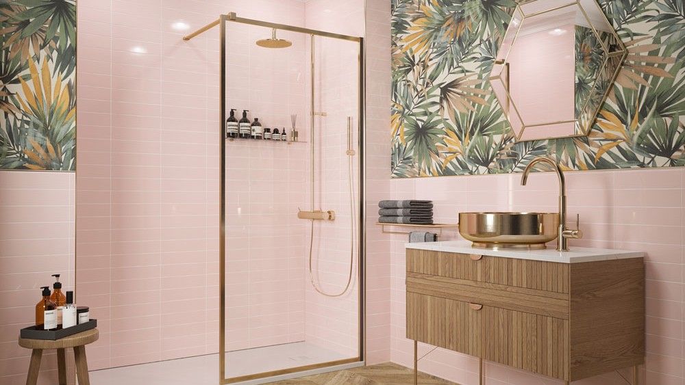 a bathroom with pink wall tiles, a green leaf patterned area on the walls with a gold trim mirror, walk-in shower and a brown chevron laminate floor