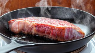 A steak cooking in a cast iron skillet on a burner