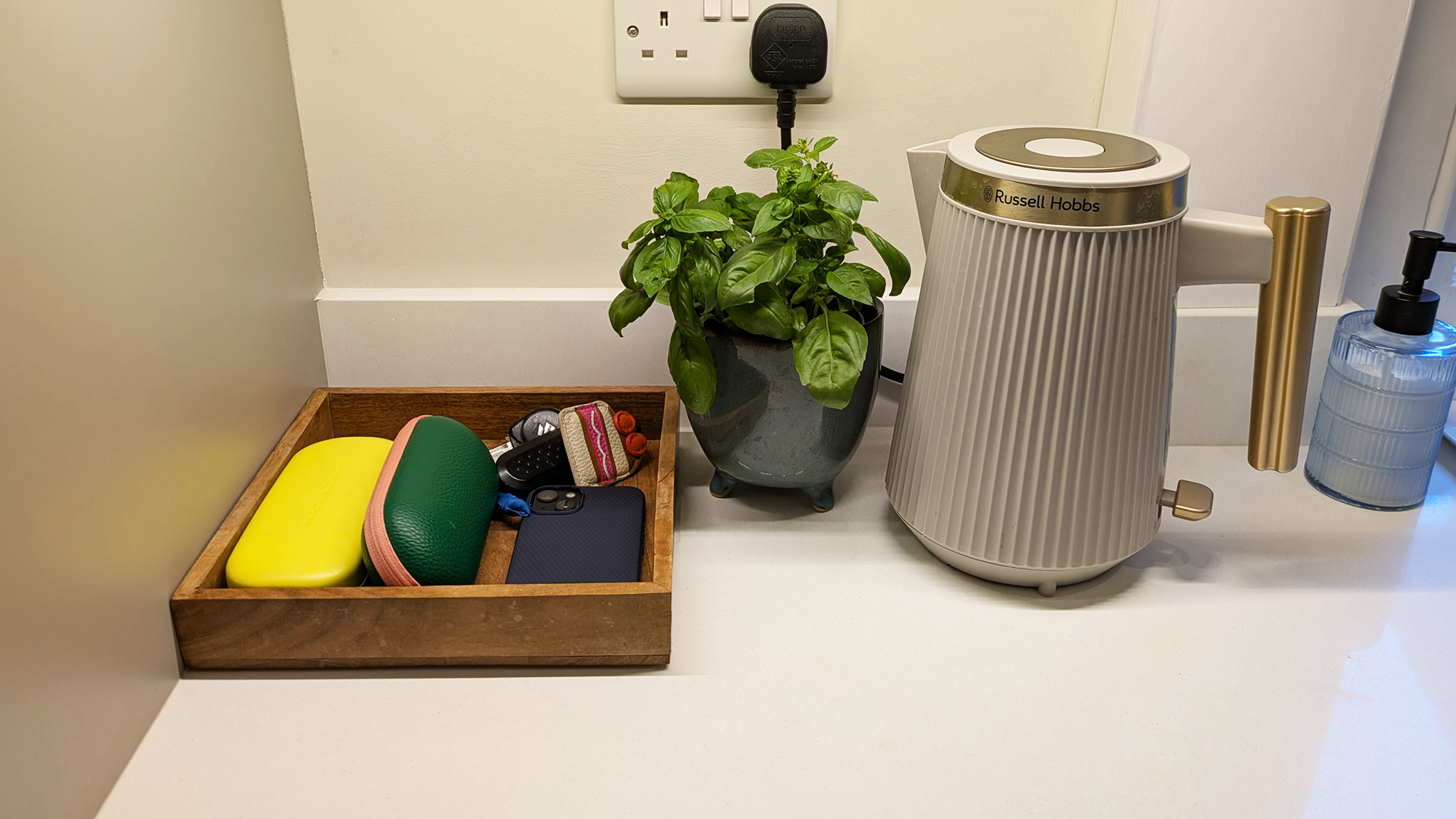 A small tray in a kitchen storing glass cases, phones and keys