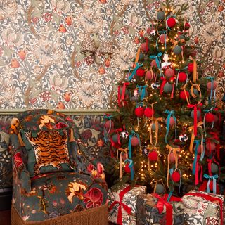Maximalist Christmas living room with orange, red and blue ribbons on tree, patterned wallpaper and matching giftwrap, upholstered chair