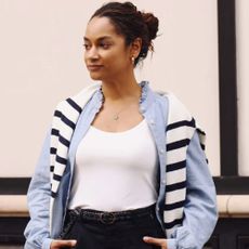 Woman wearing white t-shirt, blue overshirt and striped jumper over her shoulders, with black jeans