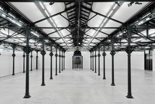 Interior of exhibition hall with white walls and floors and black pillars and trusses.