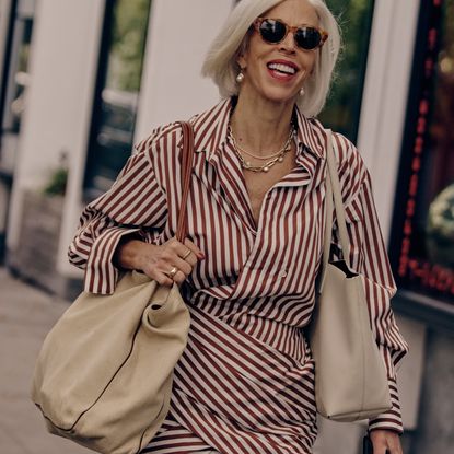 woman wearing a red and white striped poplin dress carrying a tan tote bag with sunglasses on