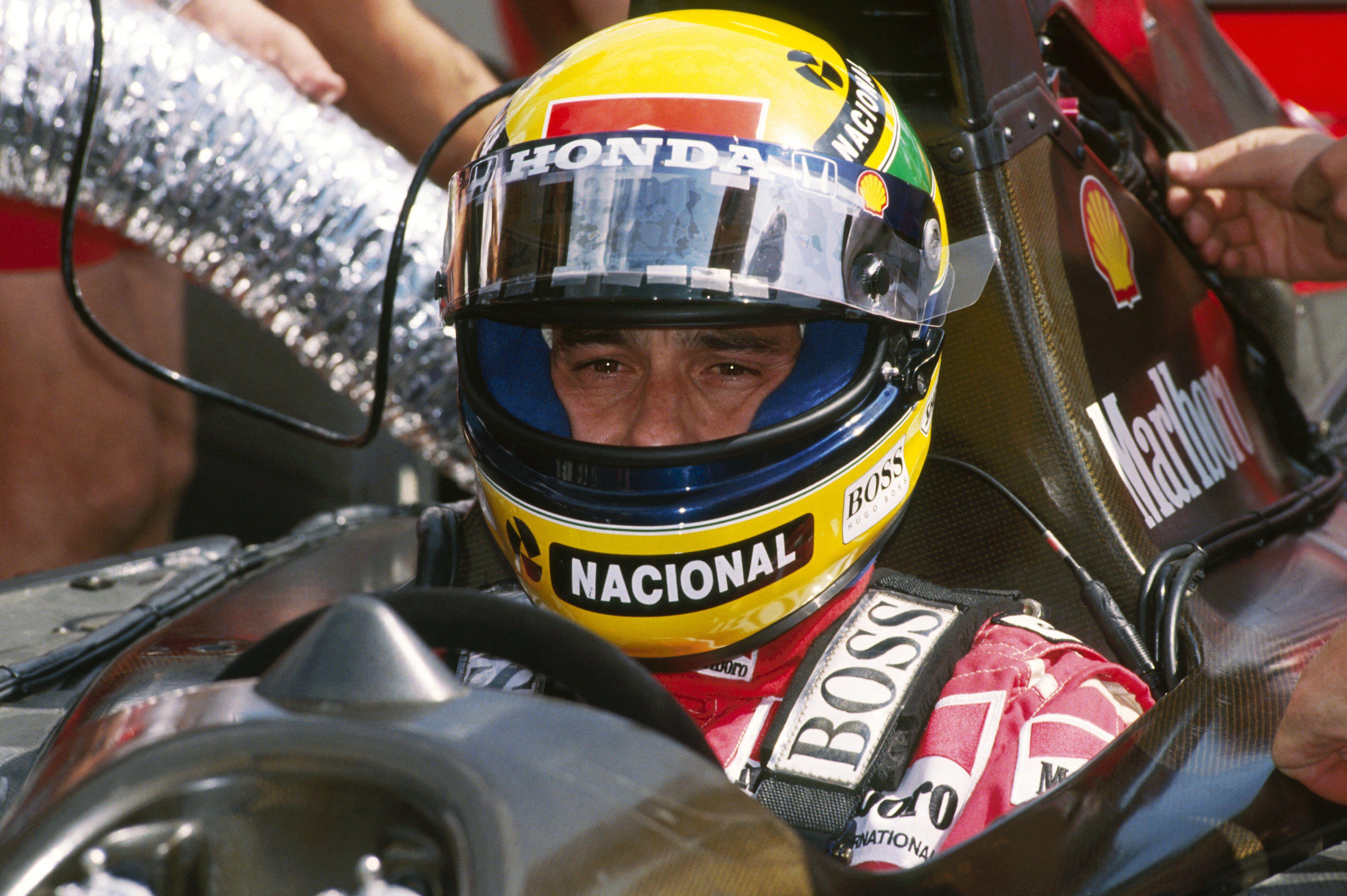Ayrton Senna sits in his racecar, face covered by his iconic yellow and green helmet.