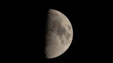 A waxing gibbous moon is seen in the night sky, with craters and dark lunar plains visible on its illuminated surface.