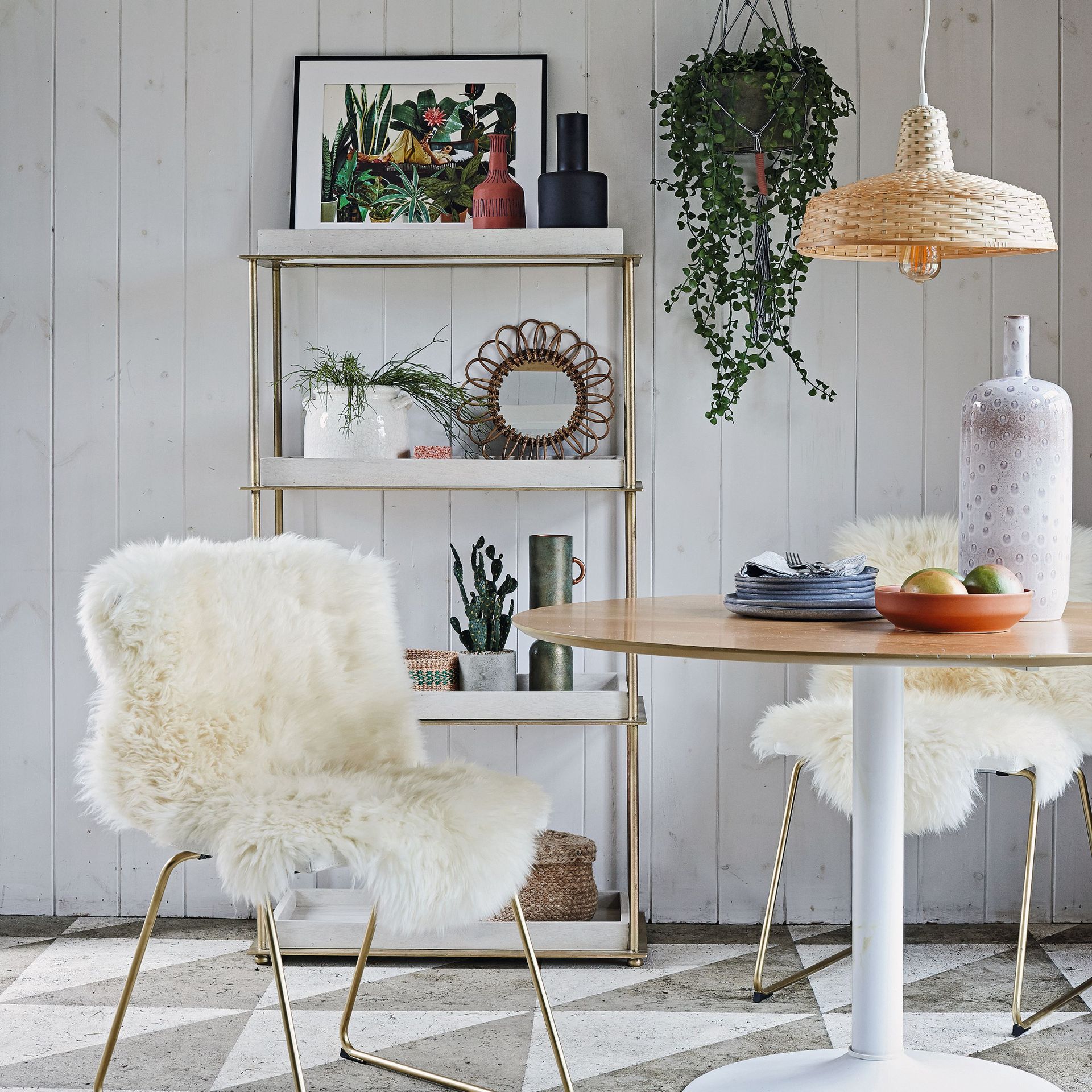Round table with a wooden top and two chairs with fluffy covers with shelf unit in the background