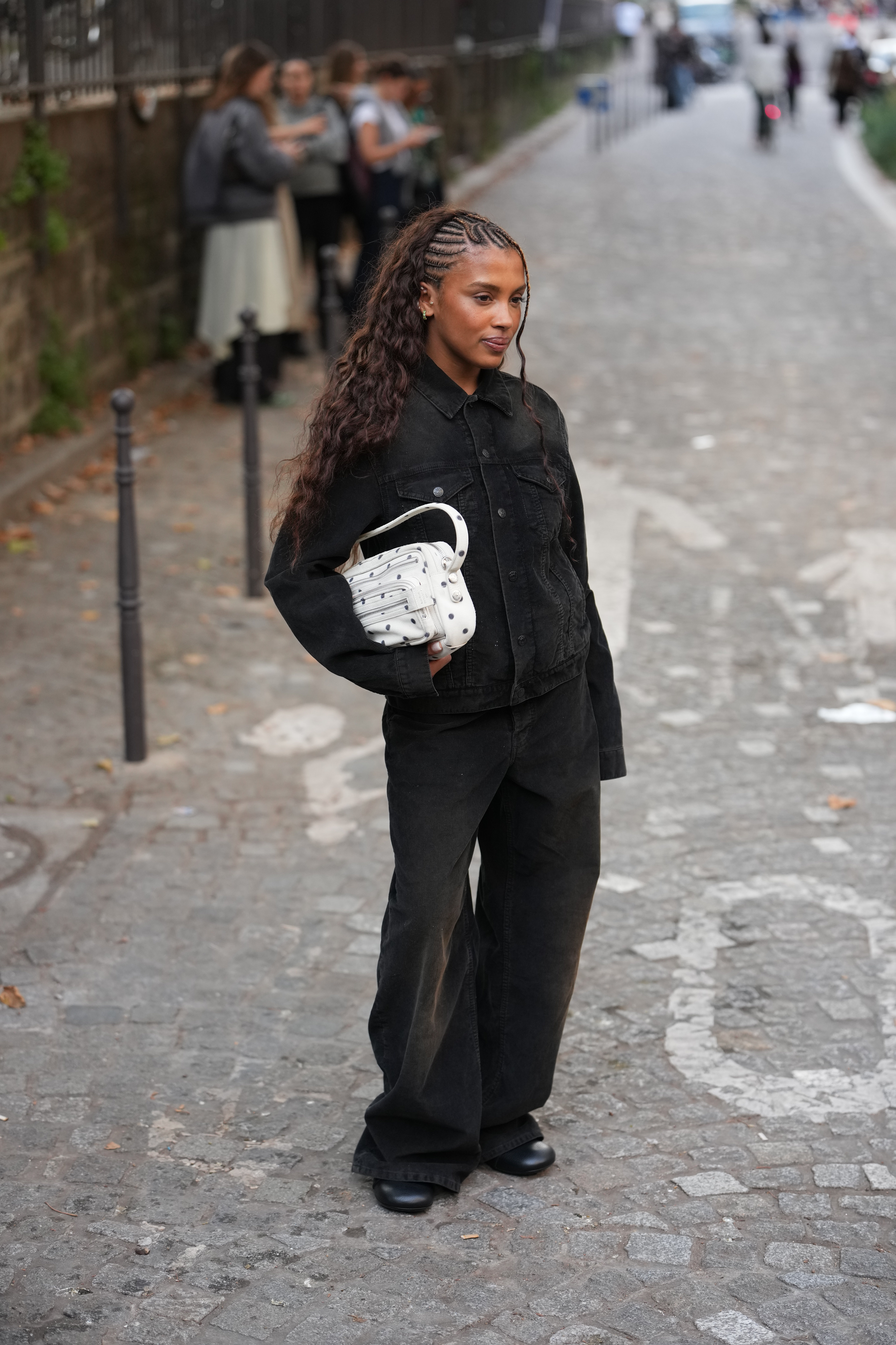 PARIS, FRANCE - OCTOBER 01: Marie-Victoire Tiangue wears long dark brown hair styled in cornrow braids at the crown flowing into loose waves, small gold hoop earrings, a handheld white leather top-handle bag with silver stud detailing, a button-front black denim jacket, black wide-leg denim jeans, black leather rounded-toe shoes, outside Acne Studios, during Paris Fashion Week - Womenswear Spring Summer 2026, on October 01, 2025 in Paris, France (Photo by Edward Berthelot/Getty Images)
