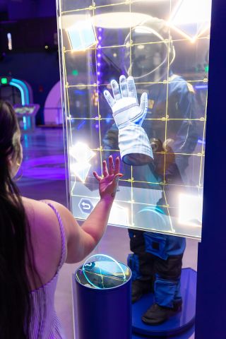 An interactive element of the replica Boeing Starliner suit display allows visitors virtually try on a glove in Gateway: The Deep Space Complex.