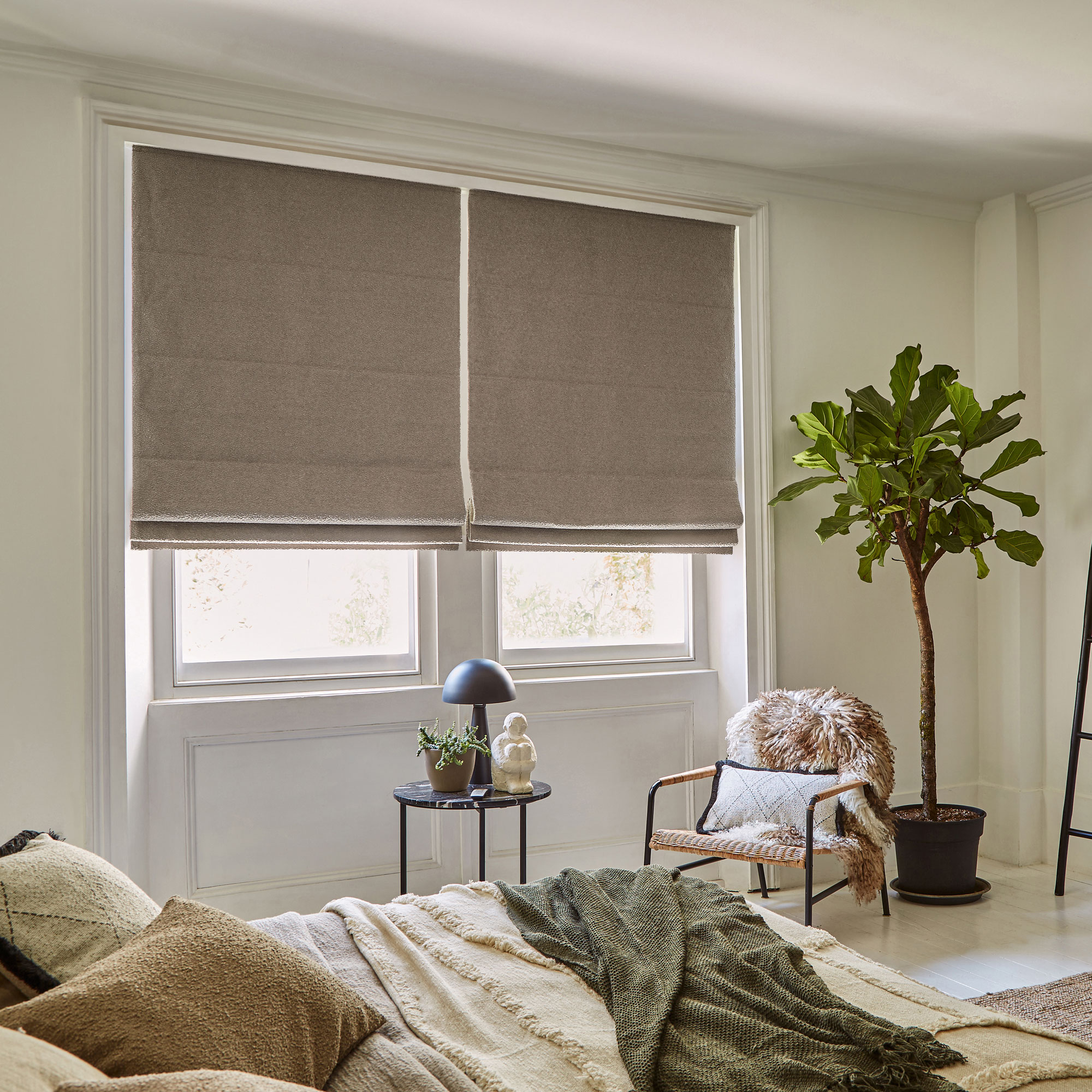 White bedroom with brown blinds and bed, black side table and a fluffy armchair