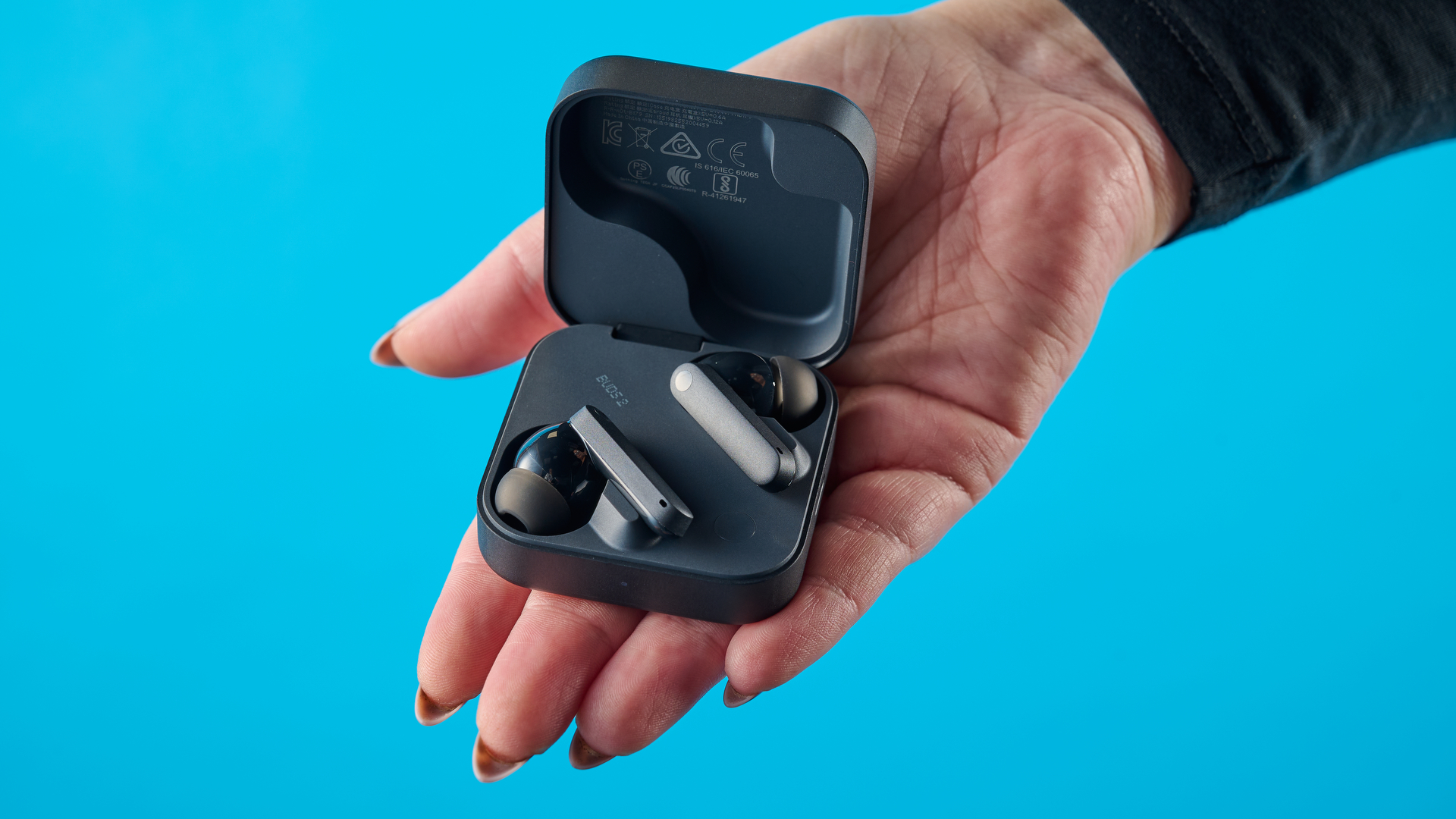 CMF Buds 2 in Dark Gray photographones on a gray table in front of a blue background