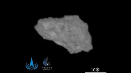 A blurry photo of an irregular-shaped grey asteroid in against the darkness of space