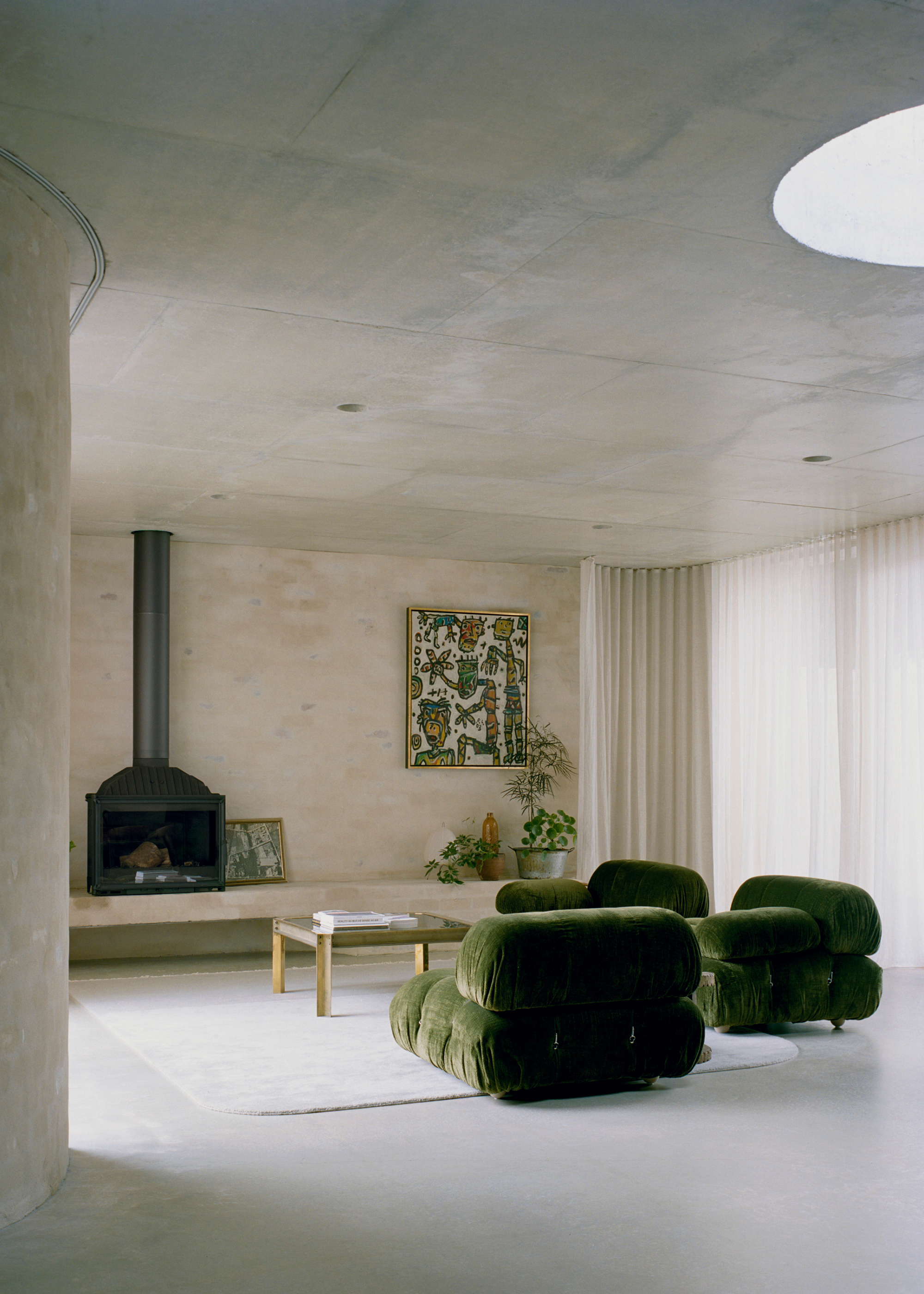 A living room with green sofa seaters, a coffee table, a floor rug, framed art, a fireplace and potted plants