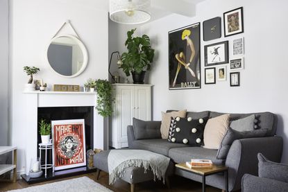 Scandi style Living room with light grey walls, original brown floorboards, grey sofa and matching footstool covered in pastel pink and black cushions and gallery wall