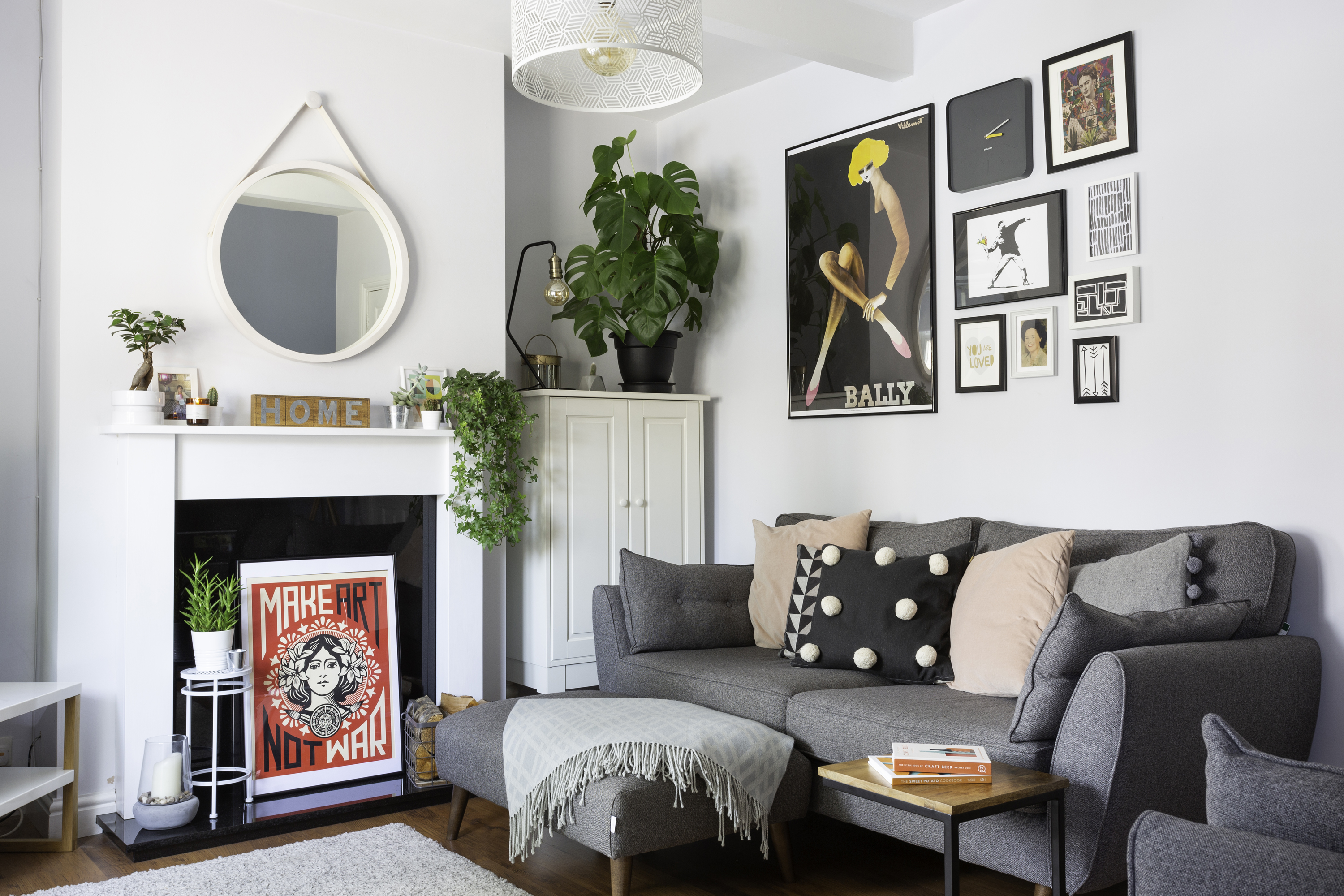 Living room with light grey walls, original brown floorboards, grey sofa and matching footstool covered in pastel pink and black cushions and gallery wall