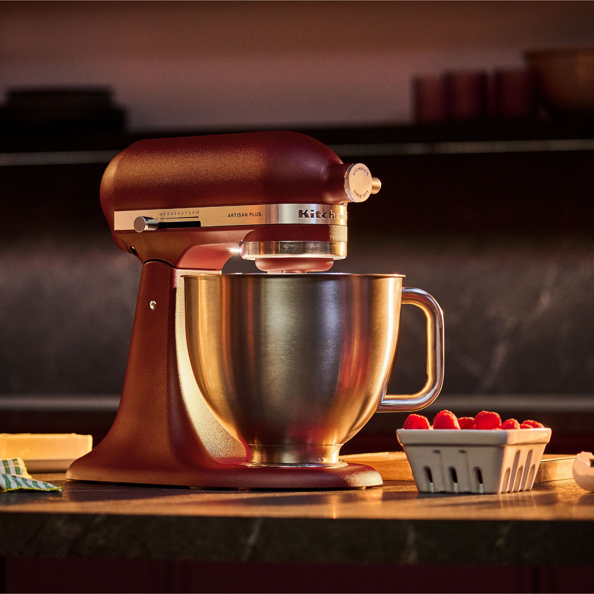 KitchenAid stand mixer in red on wooden worktop with light on, bedside raspberries