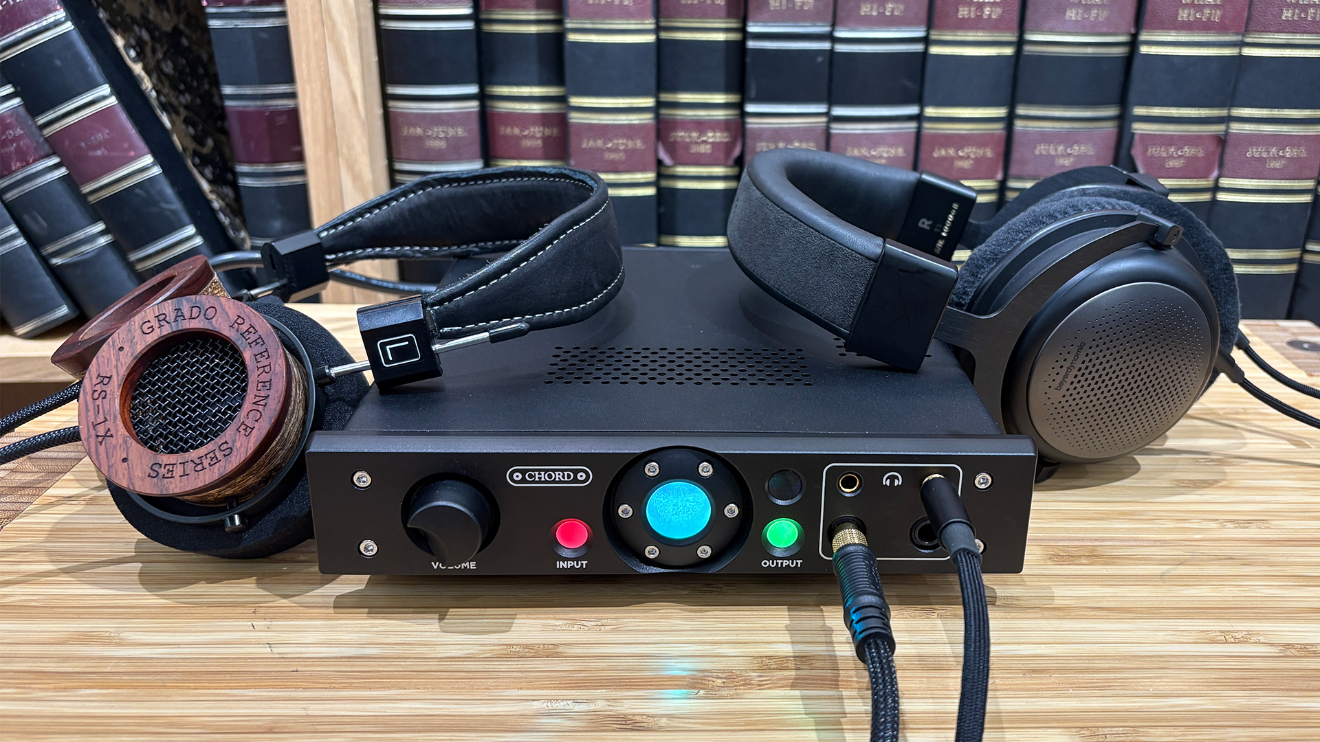 Chord Electronics Alto headphone amp on wooden surface in front of bookcase with Grado and Beyerdynamic headphones to either side