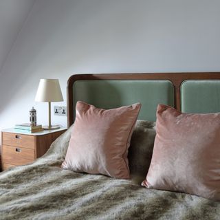 Neutral pink and green bed in bedroom with white walls