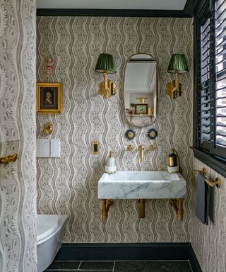 A powder room with brown and cream patterned wallpaper and green lampshade sconces