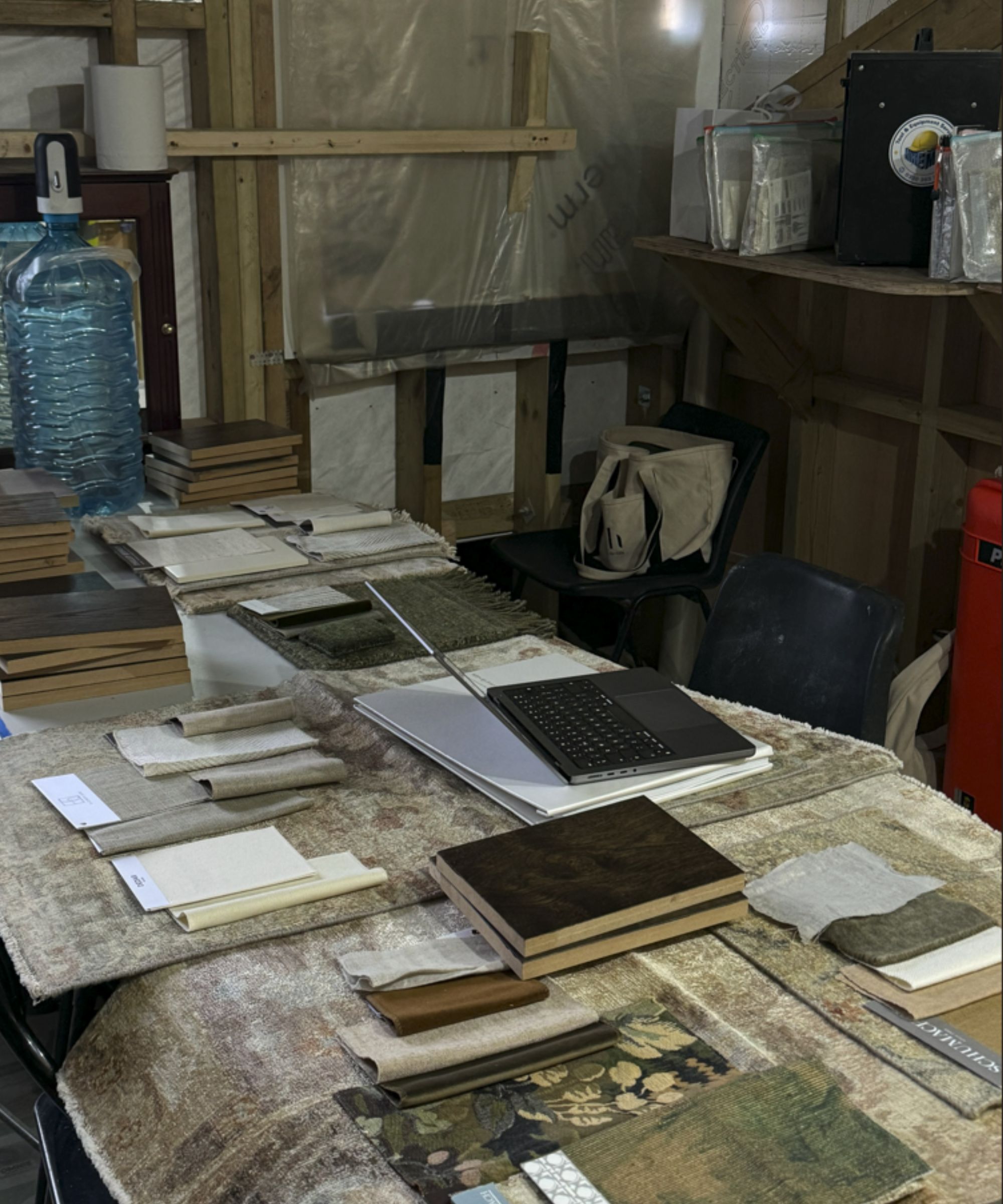 Interior designer's work station inside a home habing a renovation. Table covered in paperwork, material samples, lamptop, object wrapped in background