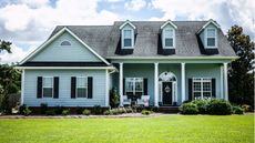 Exterior shot of large gray home with white pillars and a tidy lush lawn