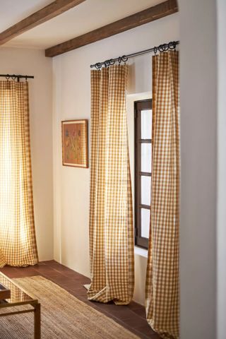 Corner shot of a living room with white walls, wooden floors, and orange-yellow gingham curtains