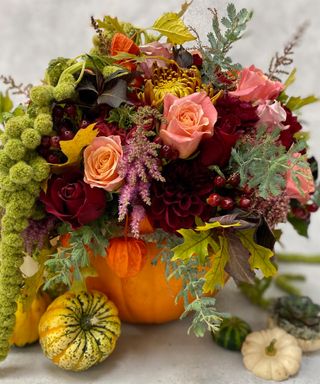 DIY Pumpkin vase ideas by Waitrose with mixed assortment of flowers including red and blush pink roses and physalis fruit with miniature pumpkins in foreground