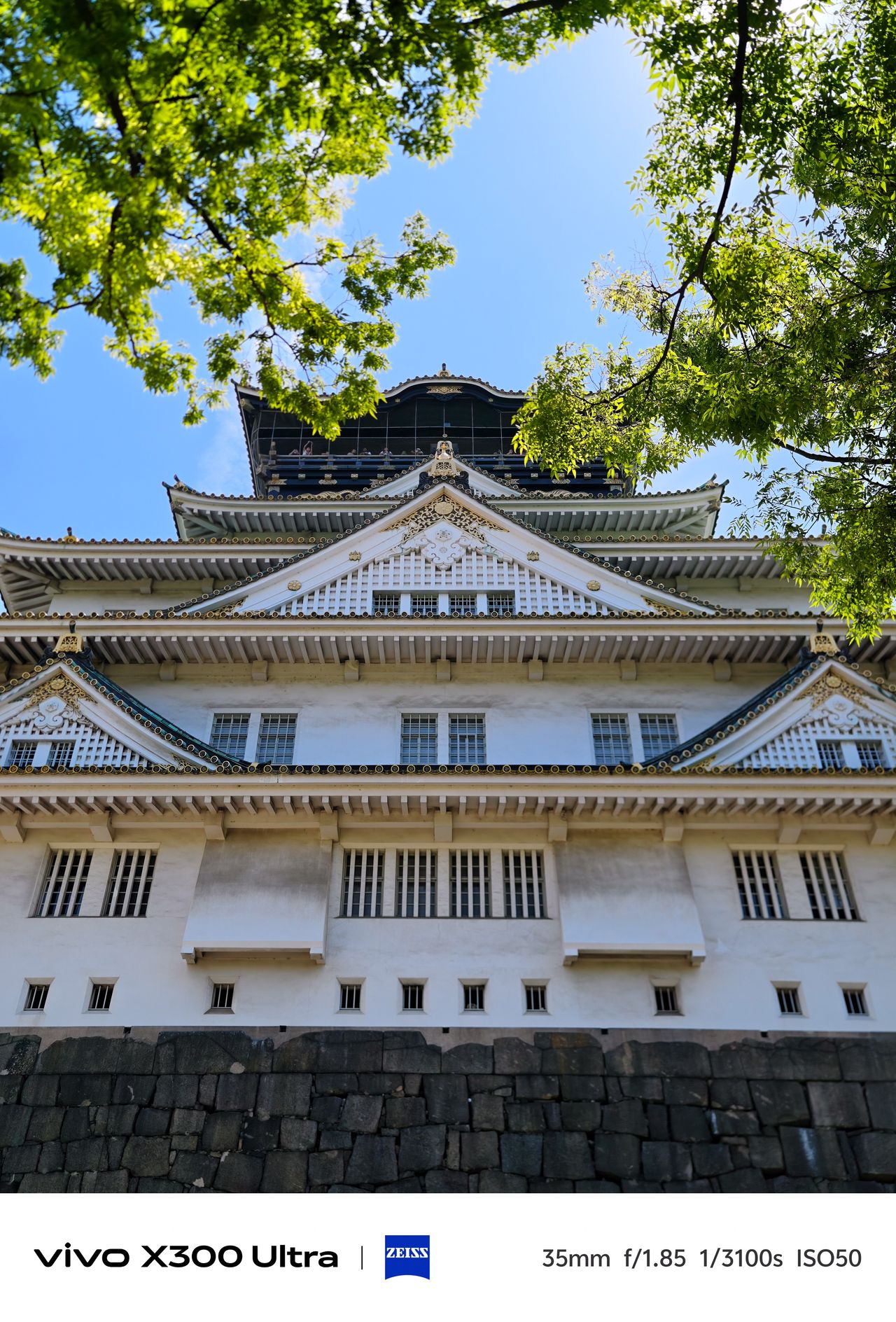 A white traditional castle structure framed by vibrant green leaves under a clear blue sky.