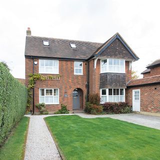 Green grass lawn in front garden with gravel path and hedging next to brick house