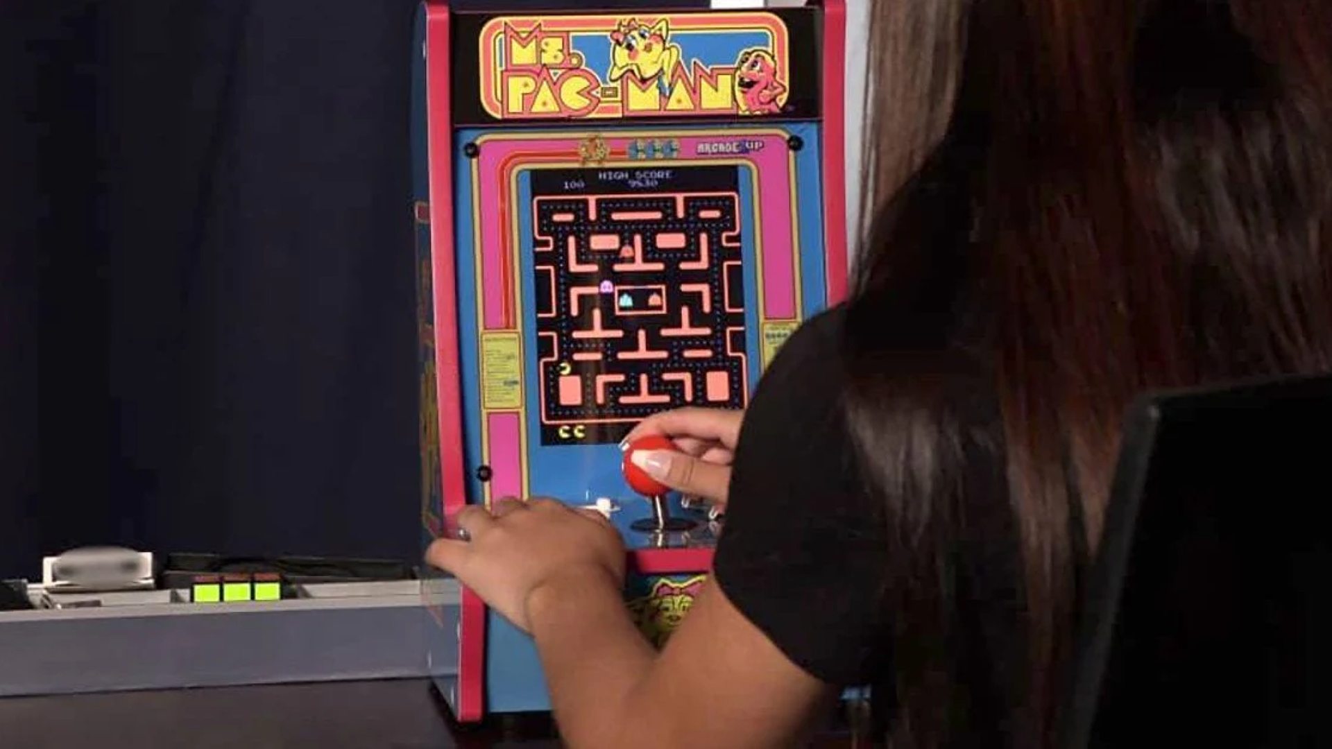 Player with long hair using Arcade1up Ms. Pac-Man arcade machine