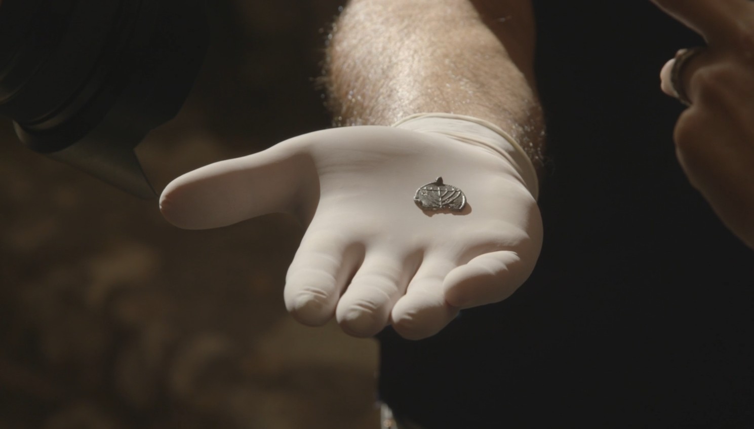 A gloved hand holds the small medallion in the palm of the hand.