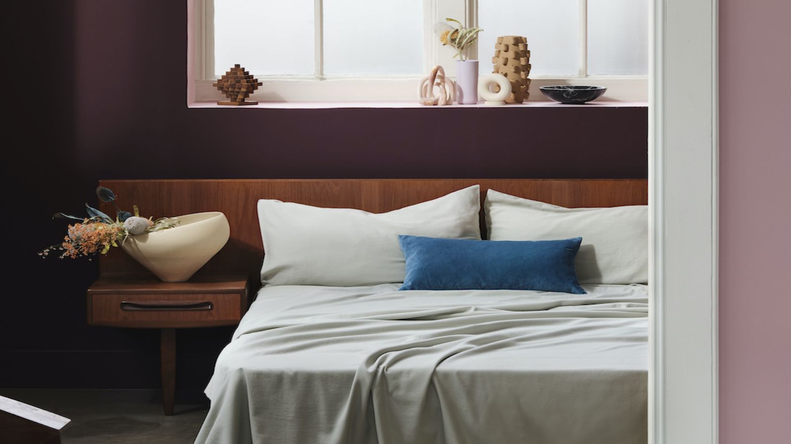 Beddable sage green bedding with a muted red wall