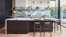 kitchen with marble backsplash and countertop, and black fluted finish with black bar stools, white walls, parquetry floors and floor-to-ceiling doors leading to the garden