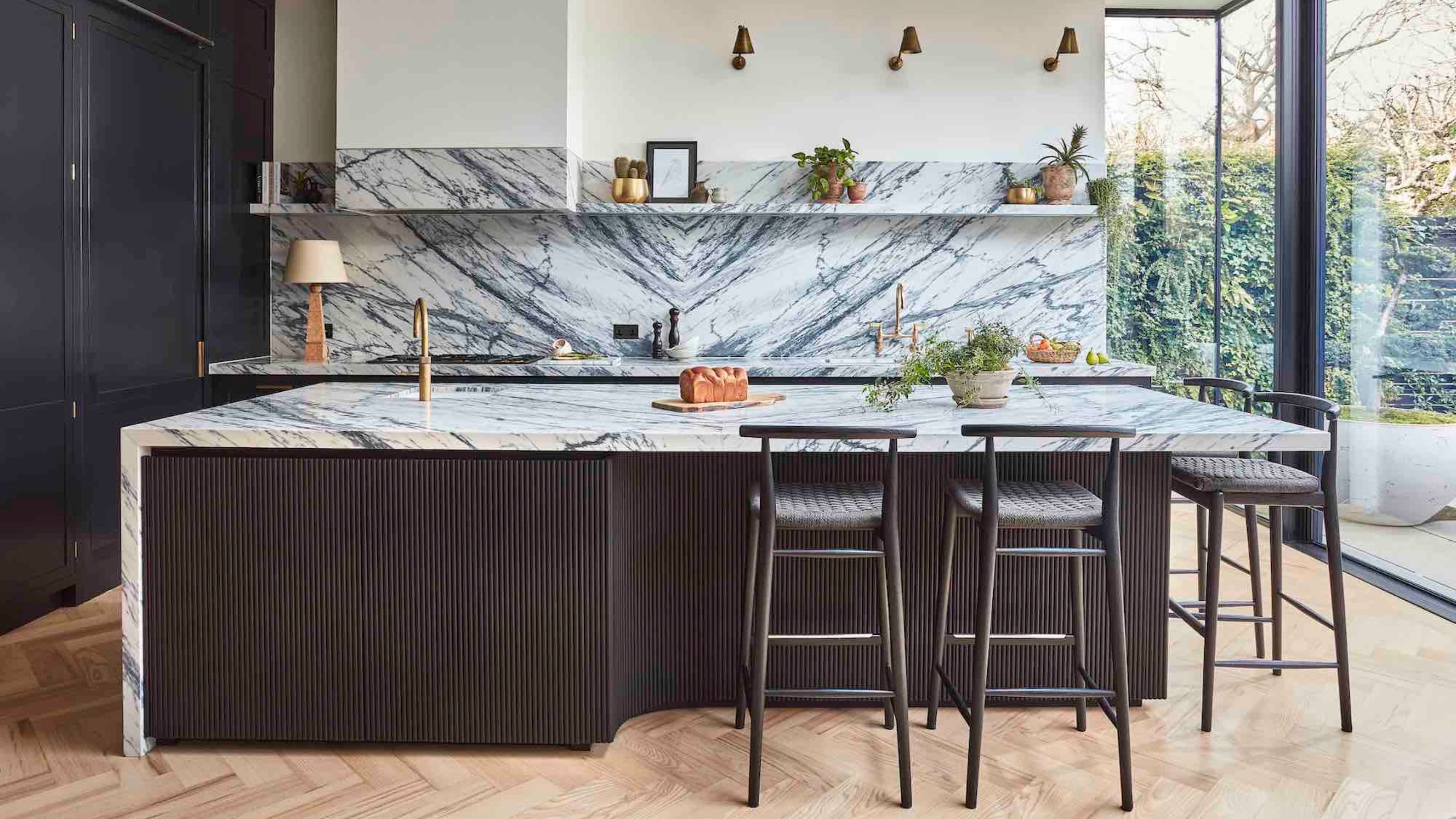 kitchen with marble backsplash and countertop, and black fluted finish with black bar stools, white walls, parquetry floors and floor-to-ceiling doors leading to the garden
