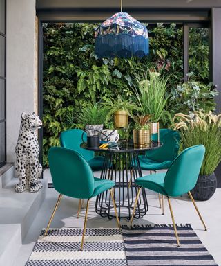 An patio dining area with green velvet chairs, pendant lampshade fixture and layered area rugs