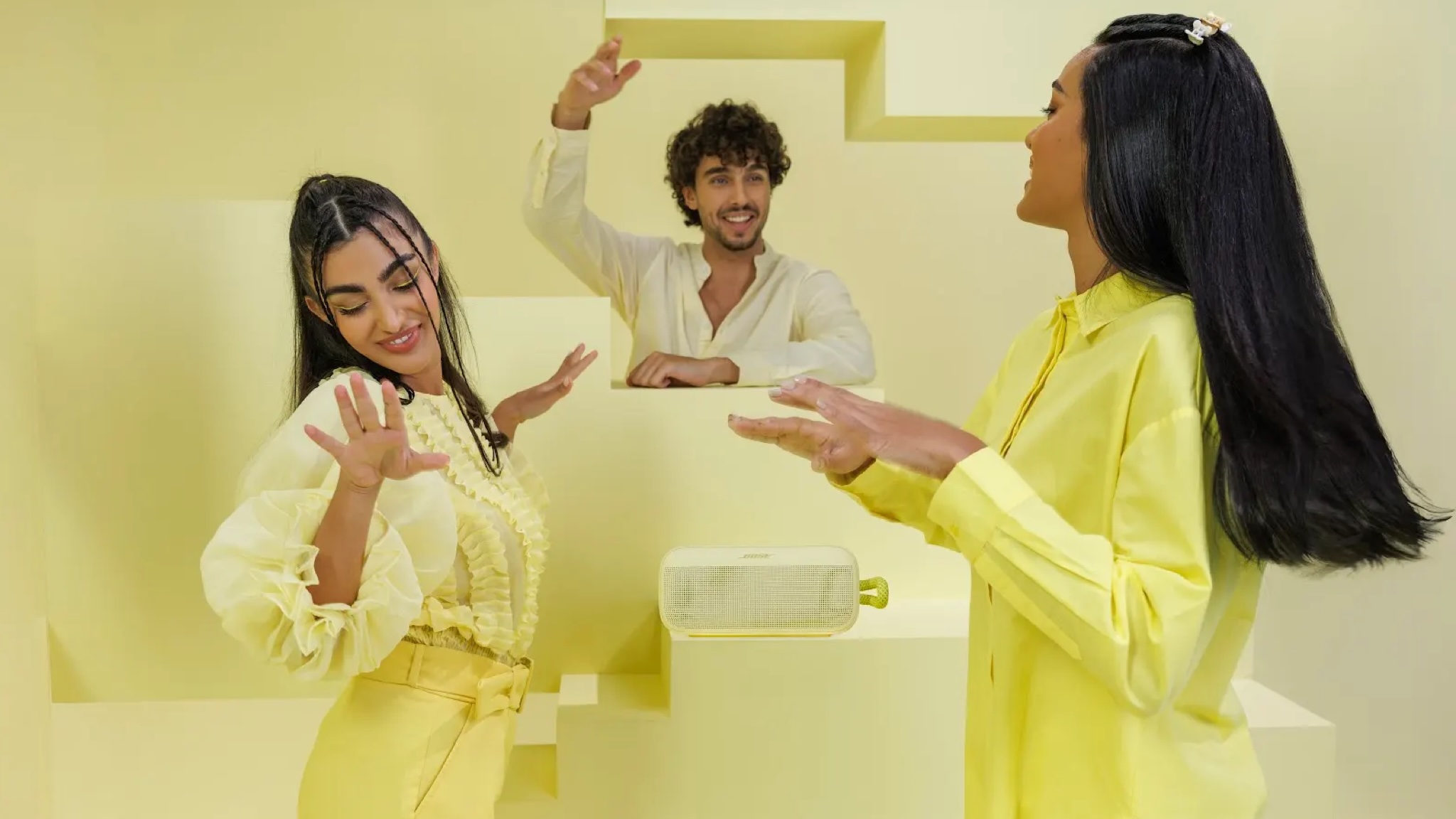 A bright summery scene showing three people in citrus yellow dancing to a Citrus Yellow Bose SoundLink Plus speaker