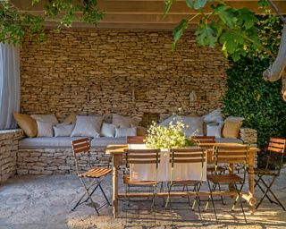 outdoor dining area with wooden table, wooden slatted chairs and stone sofa with cushions