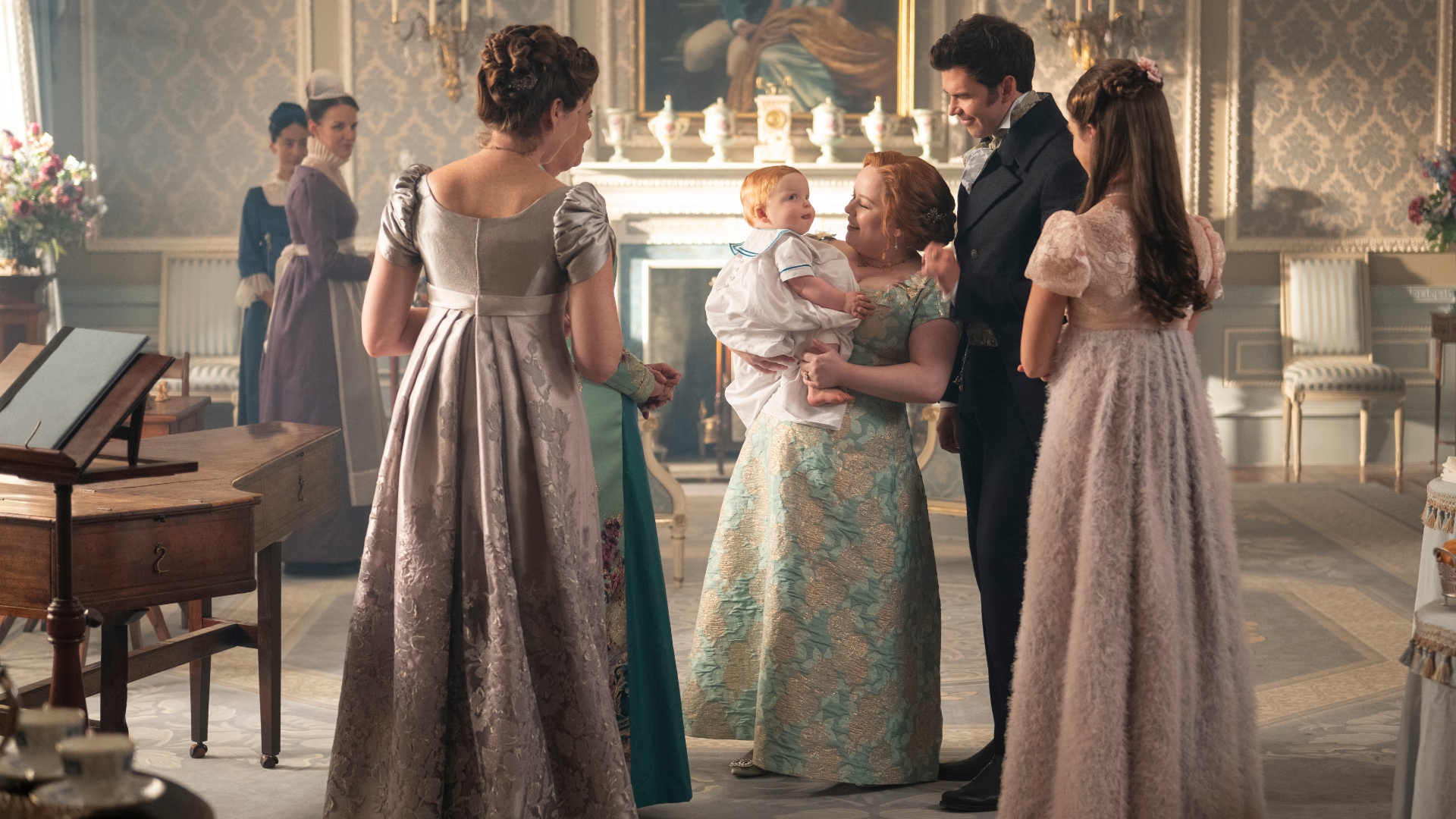 The Bridgerton's stand around Penelope and Colin holding their baby in Bridgerton season 4