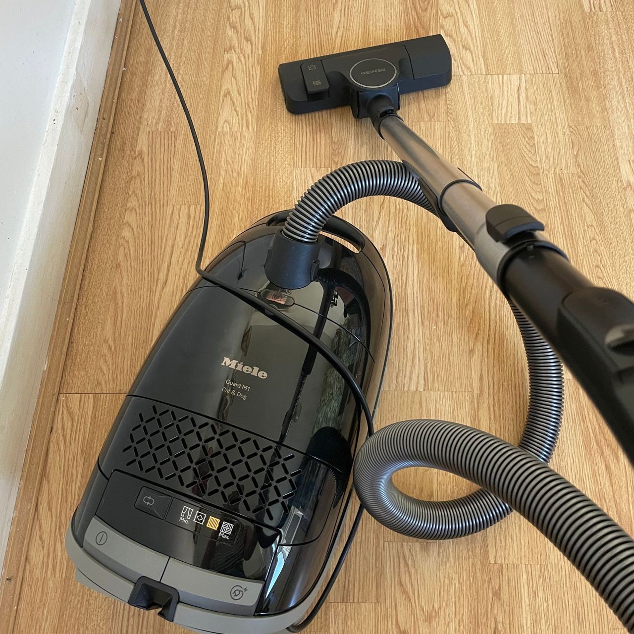 Black Miele cylinder vacuum, cord and nozzle on hardwood floor