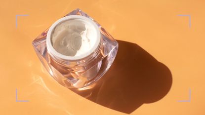 Pot of skincare cream containing ceramides on an orange backdrop with a shadow