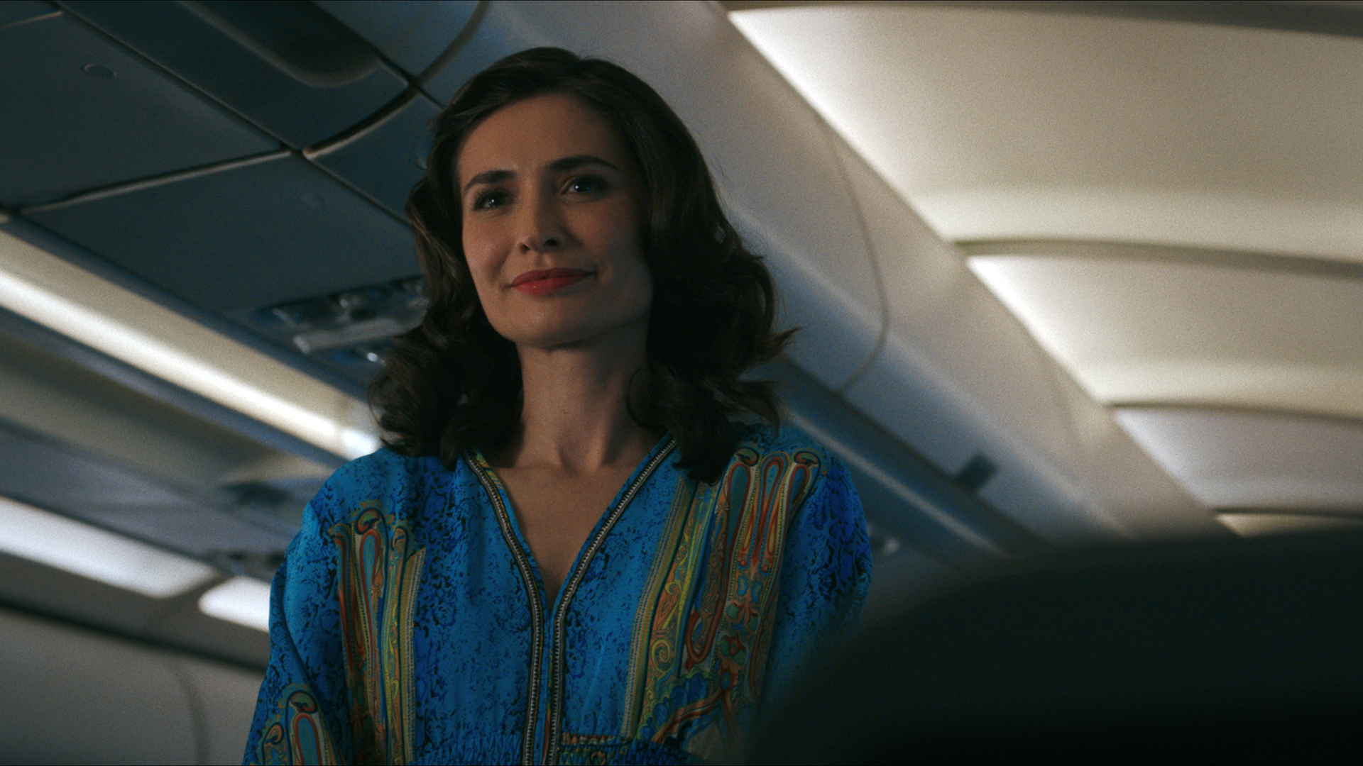 Zosia standing and smiling in an airplane in Pluribus episode 3