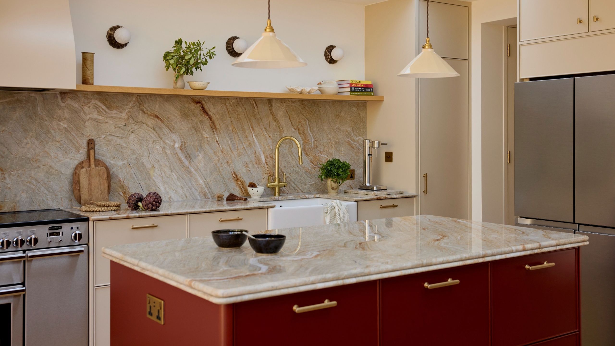 A modern kitchen with a kitchen island with a bullnose counter and red cabinets with beige cabinets in the rest of the space and the same countertop stone running along the backsplash