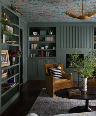 A green library with gold chairs and floor-to-ceiling shelves