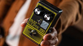 A photo of a hand holding a 50th anniversary DOD OD/Preamp 250 pedal 