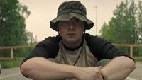 A man in a green bucket hat, sitting on the ground in The Long Walk