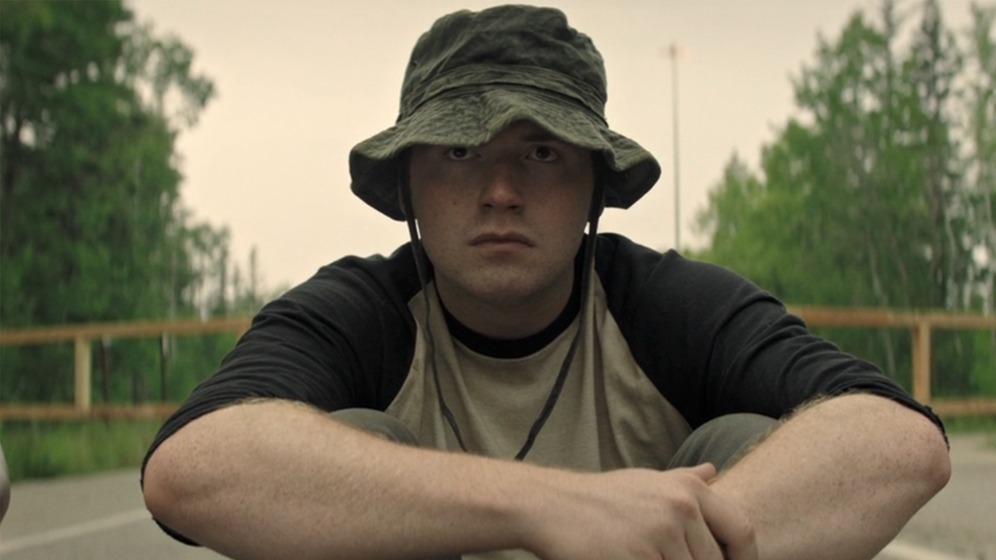 A man in a green bucket hat, sitting on the ground in The Long Walk