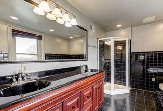 An old dated bathroom with black tiles and wooden cabinetry