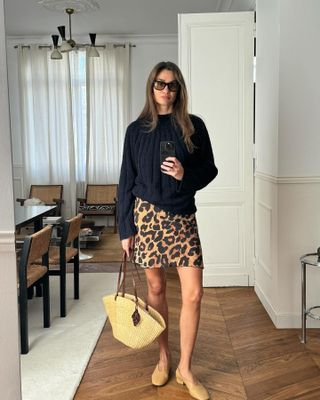 woman wearing leopard skirt and woven bag in her home
