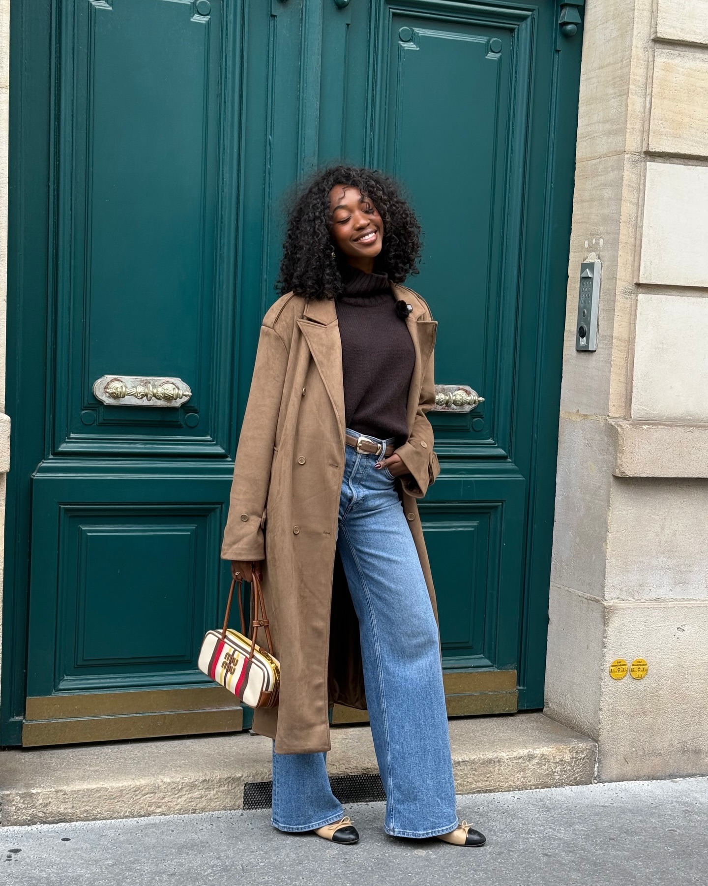 French woman wearing trench coat, brown weighty sweater, straight leg jeans, and leather ballet flats in Paris.